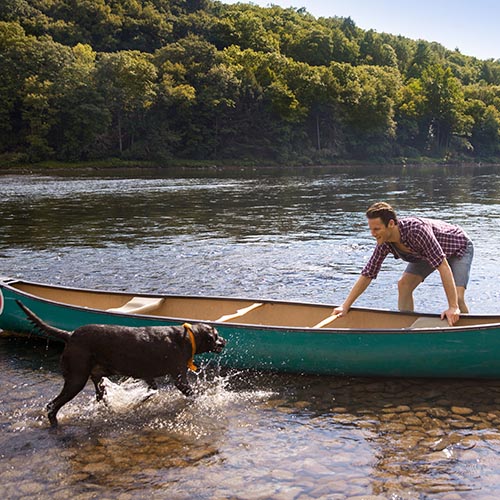 Man standing looking at dog while standing by canoe in lake